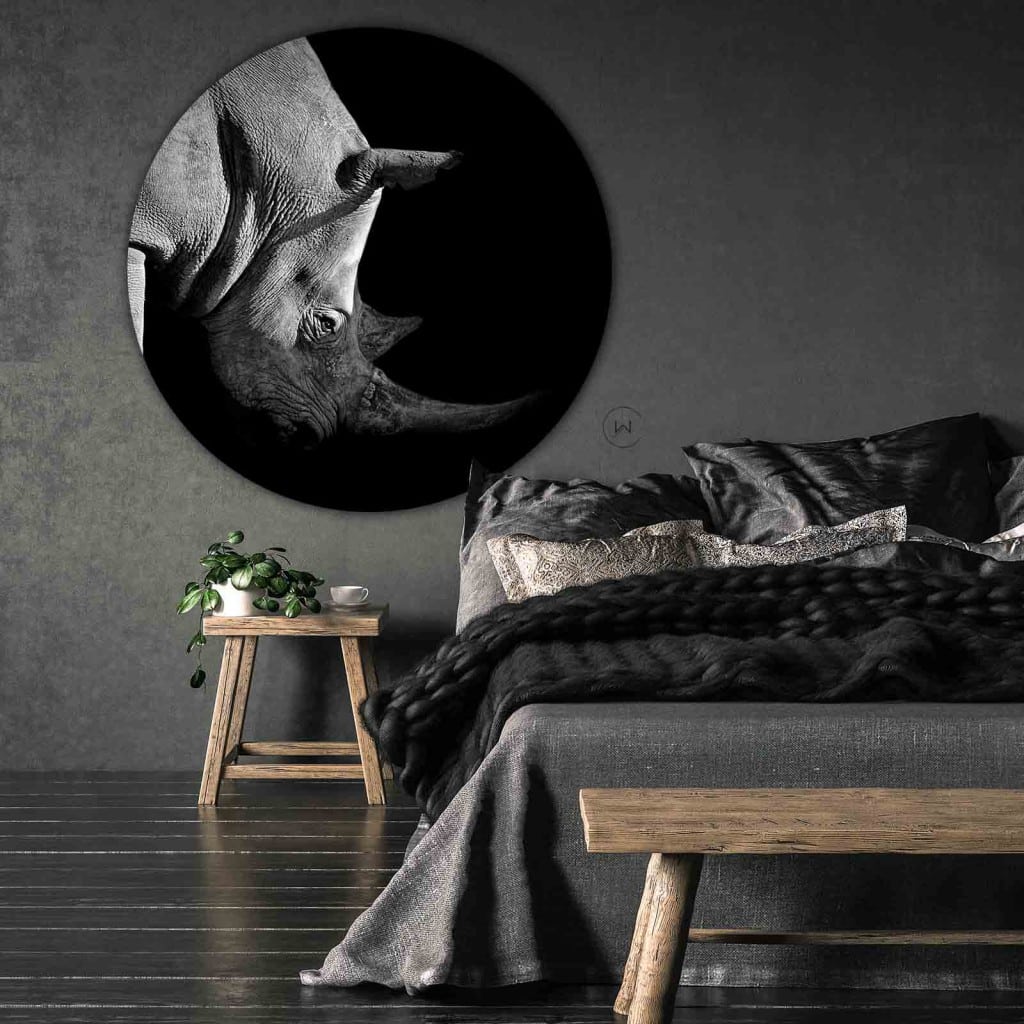 Muurcirkel neushoorn in zwart-wit aan een donkergrijze wand boven een bed met een grofgebreide plaid