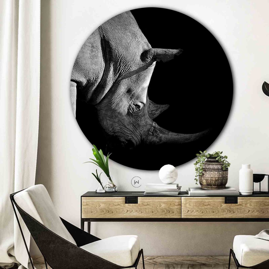 Muurcirkel neushoorn aan een witte wand boven een houten sidetable naast een witte fauteuil