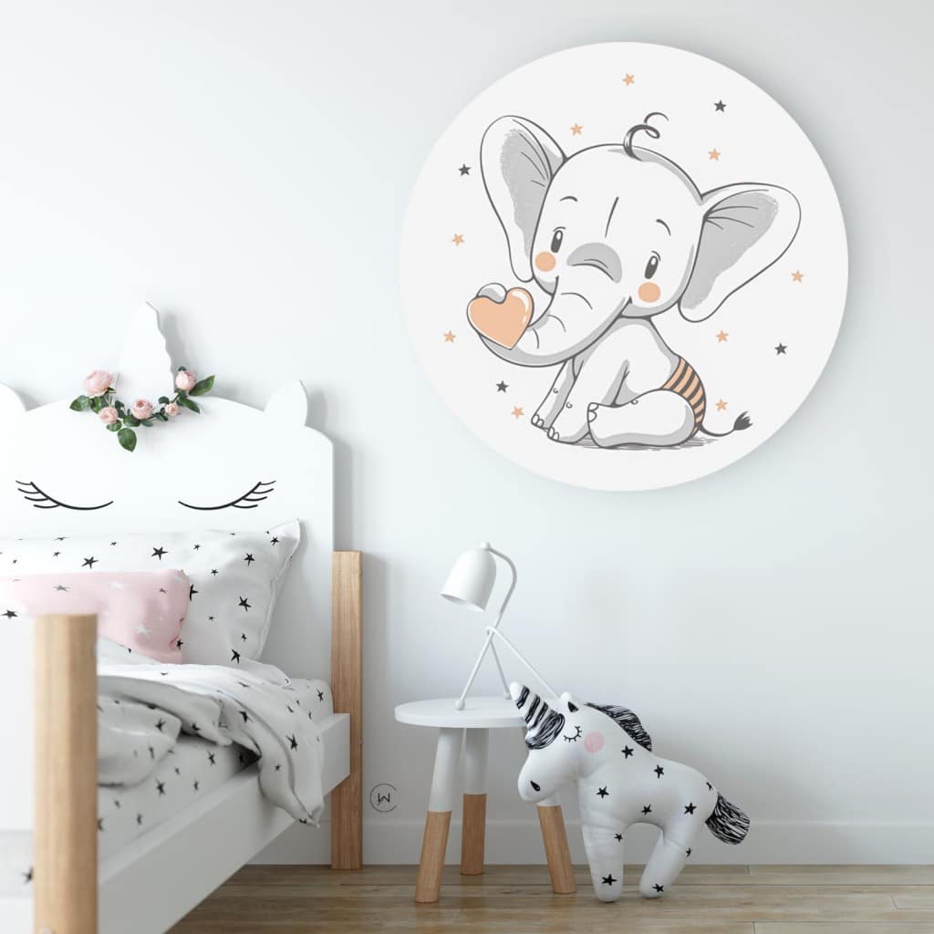 Muurcirkel babyolifant aan een witte wand in een kinderkamer boven een wit bed en een knuffelpaard