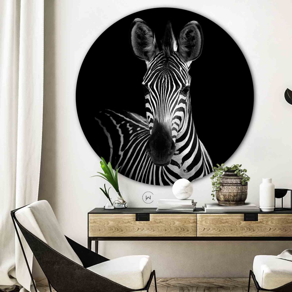Muurcirkel zebra portret aan een witte wand boven een houten console met een witte fauteuil