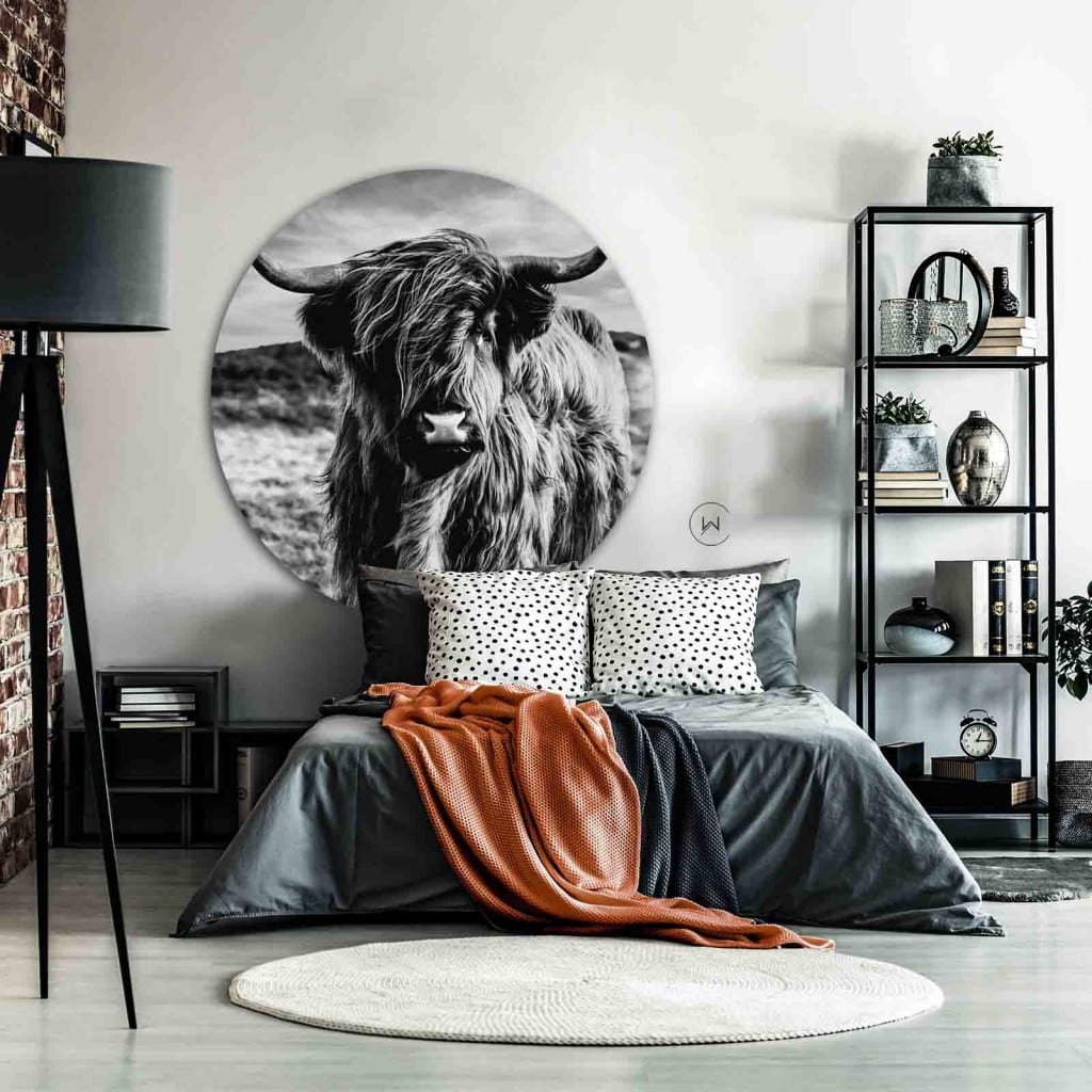 Muurcirkel Schotse hooglander zwart wit boven een bed met grijs dekbed en roestoranje plaid