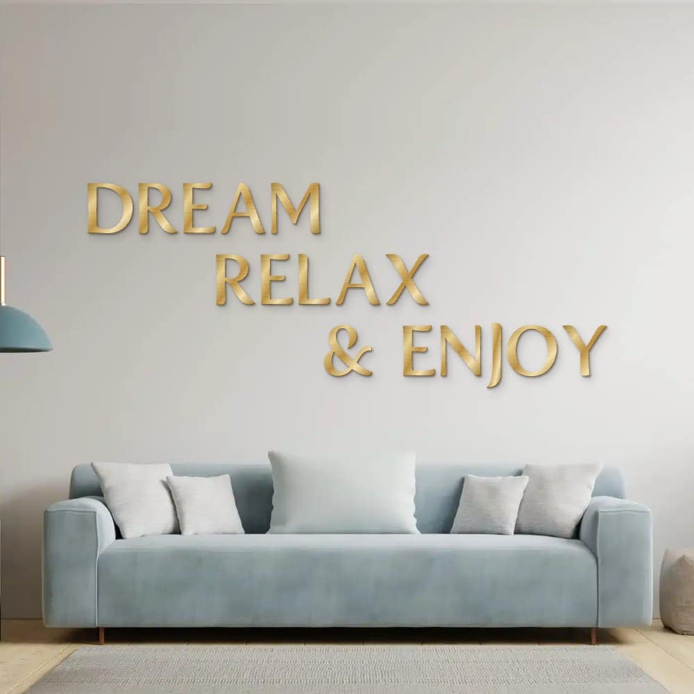 Dream Relax & Enjoy in goud geborsteld aluminium aan de muur boven een bank
