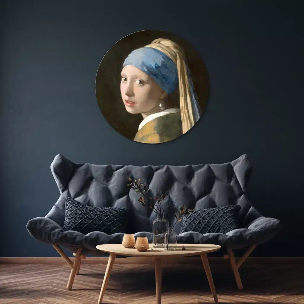 Muurcirkel het meisje met de parel van Vermeer boven een grijze gecapitonneerde bank tegen een donkerblauwe muur
