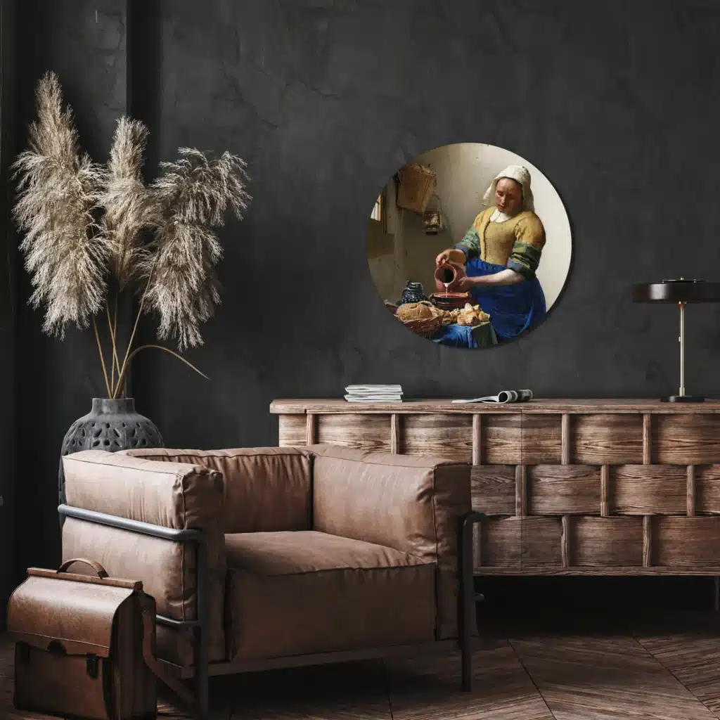 Muurcirkel het melkmeisje van Vermeer boven een houten dressoir en een leren fauteuil tegen een donkere wand