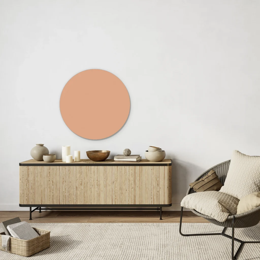 Muurcirkel licht nude pink boven een houten lamellendressoir met een loungestoel tegen een witte muur