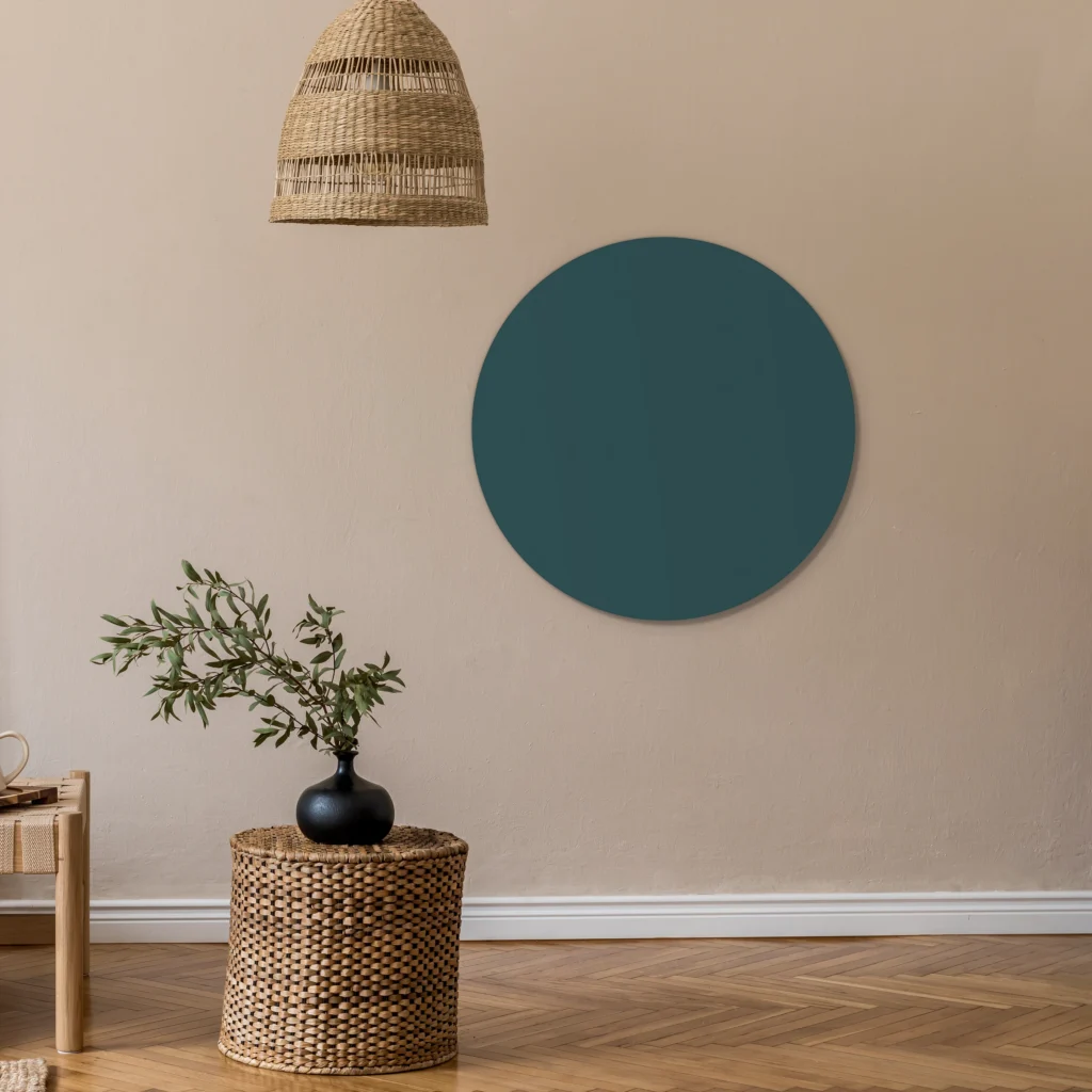 Muurcirkel petrol aan een zandkleurige wand onder een rieten hanglamp, met een plant op een rieten krukje