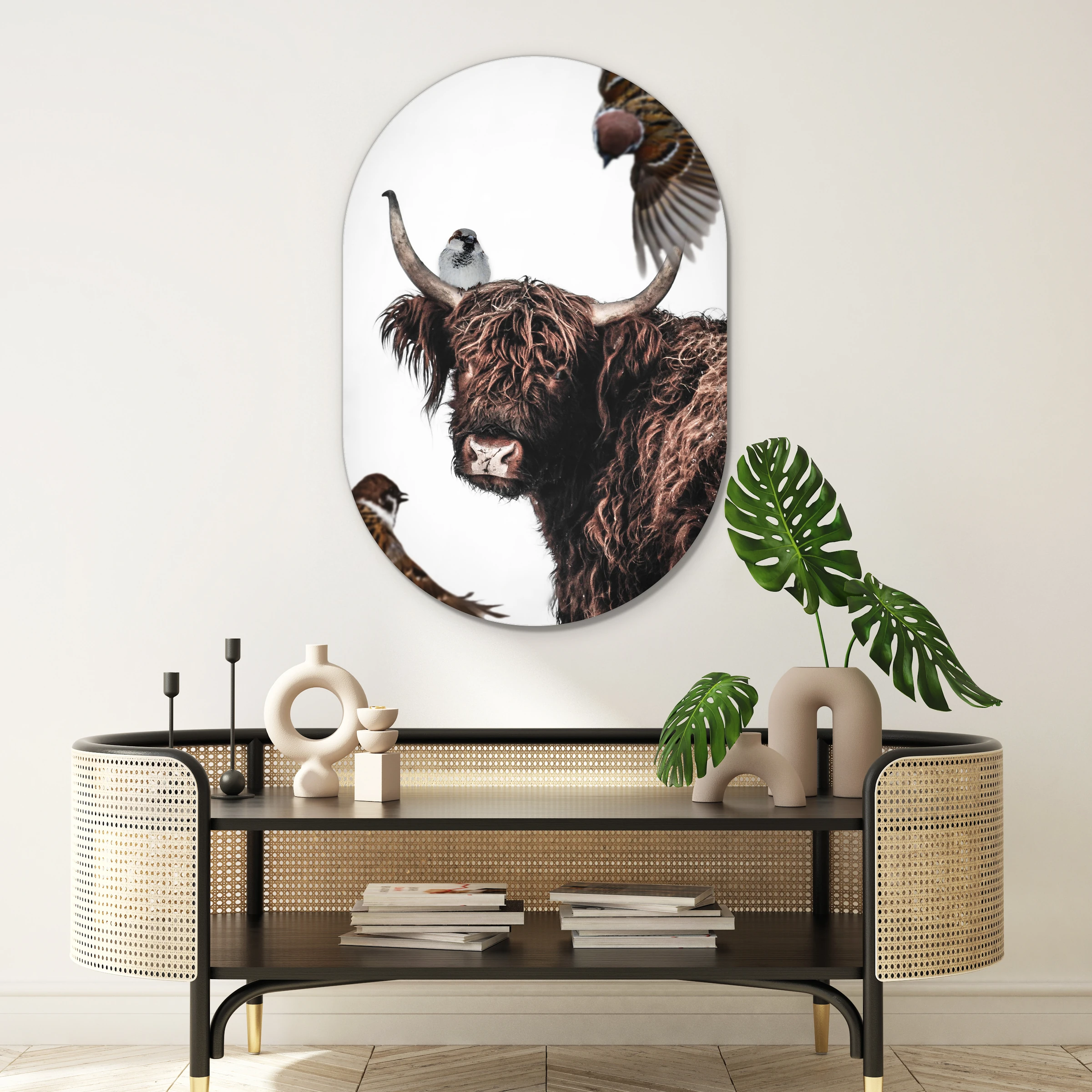 Muurovaal hooglander artistiek boven een zwarte rotan console met een monstera