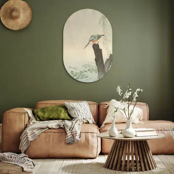 Ijsvogel schilderij als muurovaal aan een olijfgroene muur boven een cognackleurige bank