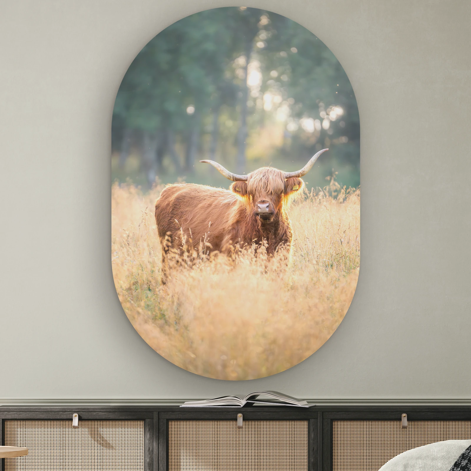 Muurovaal Schotse hooglander zonsondergang aan de muur boven een dressoir met rotan deurtjes