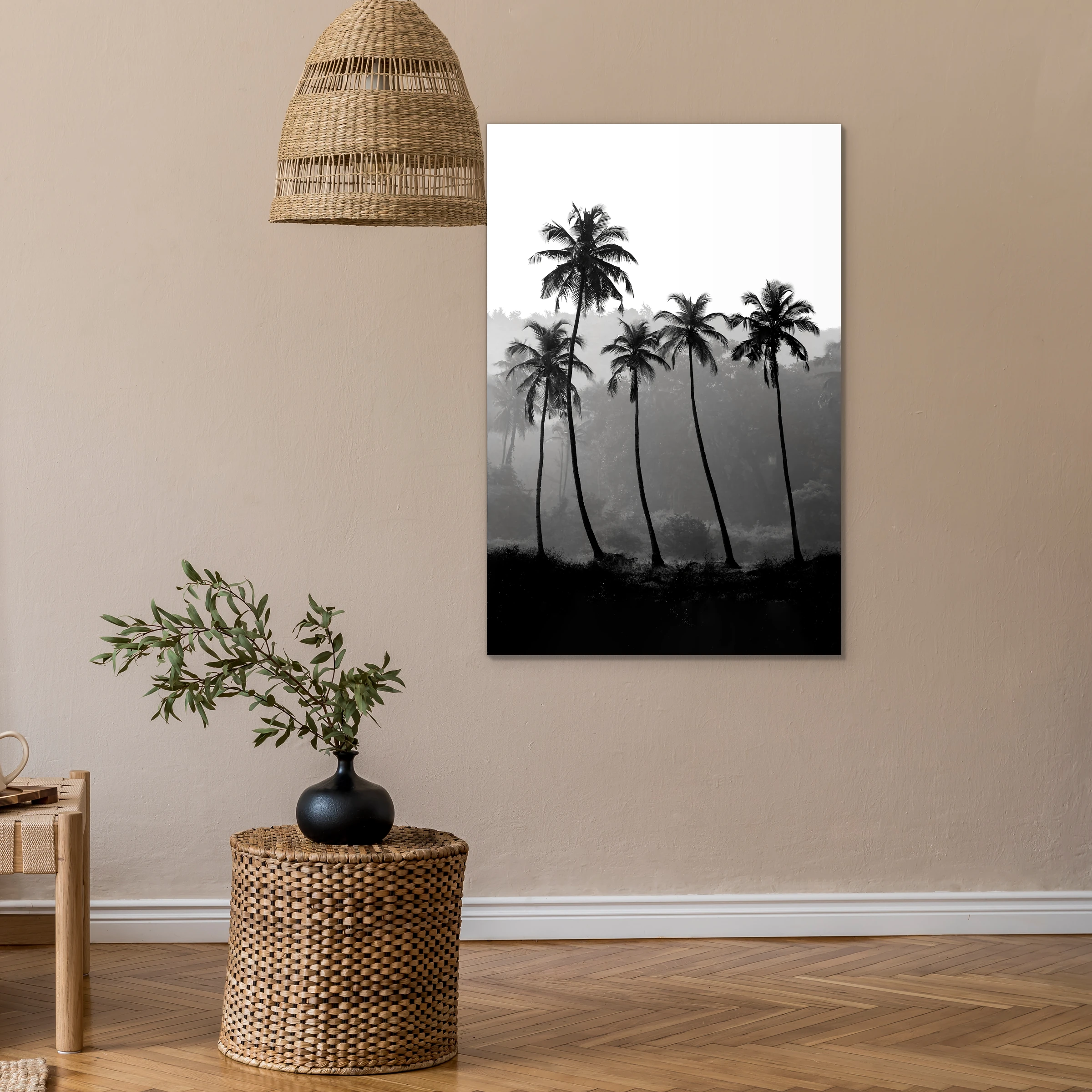 Palmbomen in zwart-wit aan een beige muur onder een rieten hanglamp, met een rieten bijzettafel